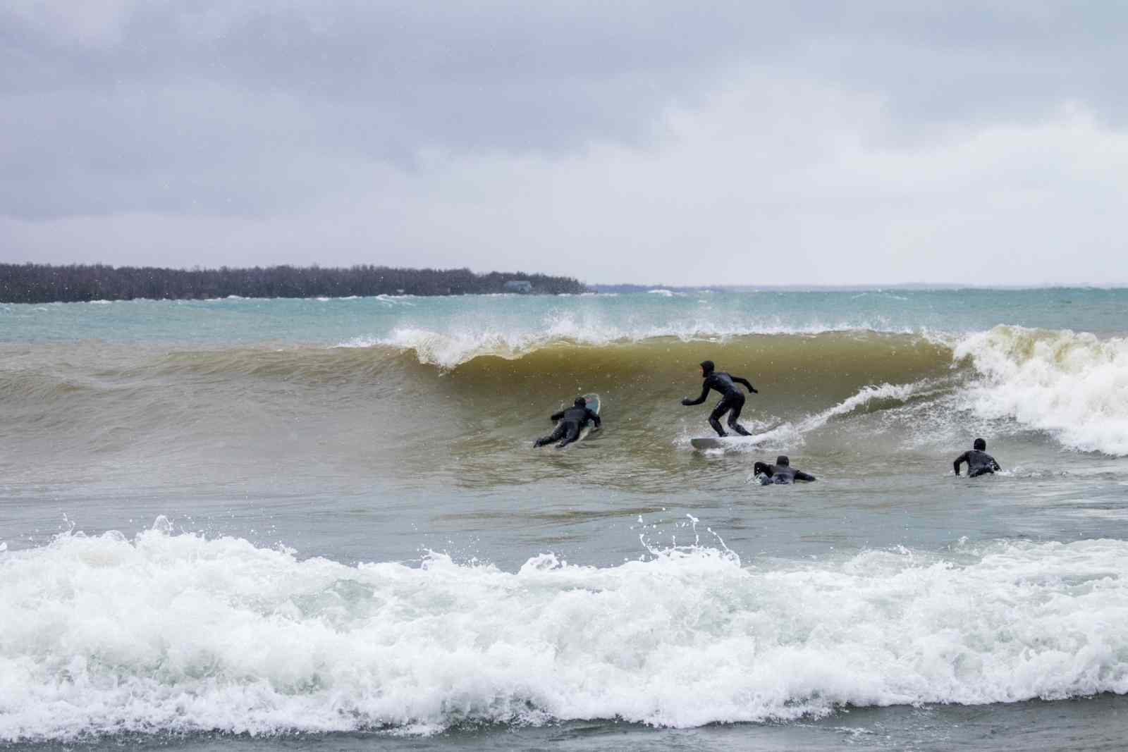 A group of people in wetsuits surf on a Great Lake in Winter