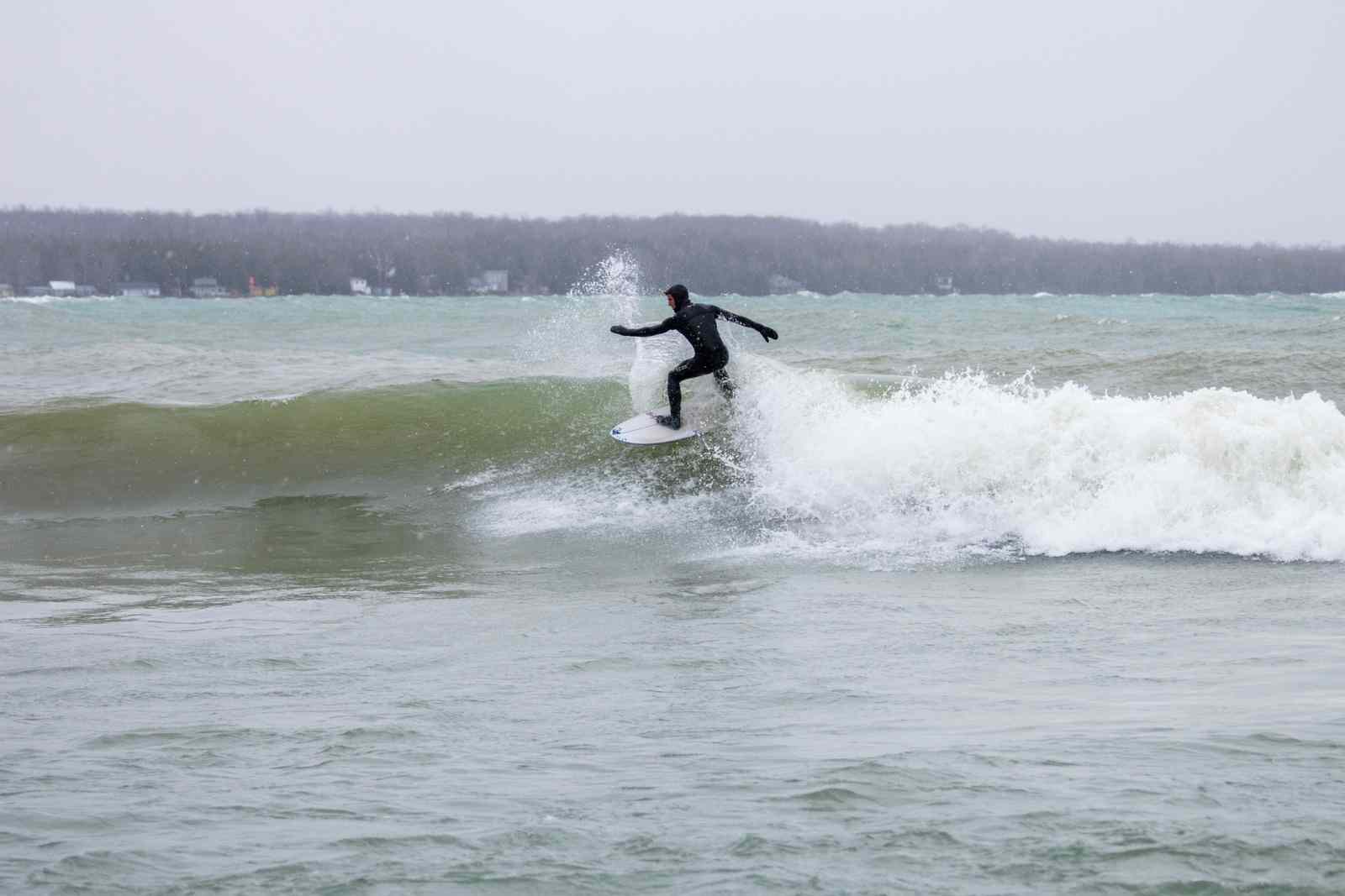 Man in a wetsuit surfs on a Great Lake in winter