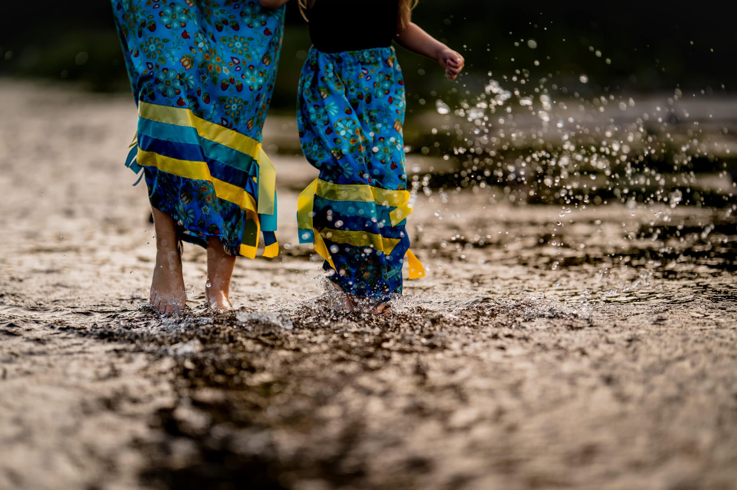 A woman and girl run through the water in matching blue ribbon skirts