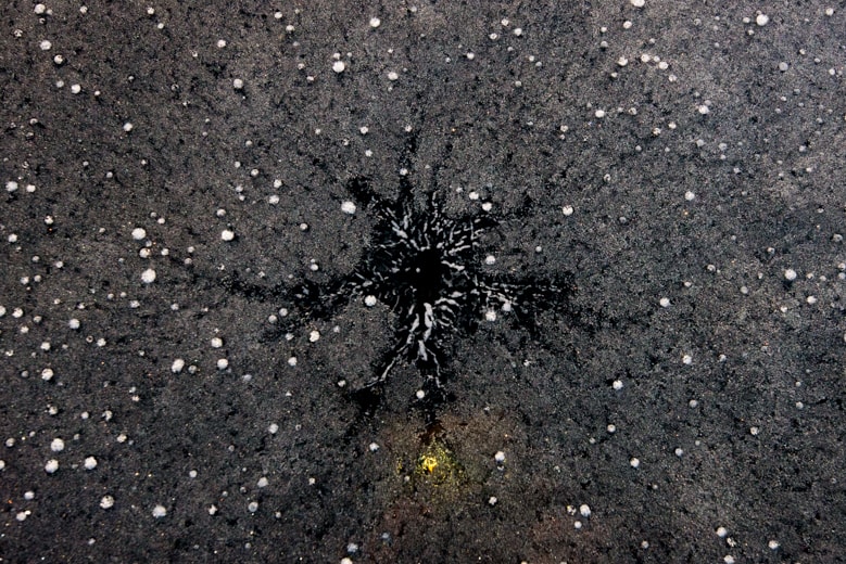 An alien-like black ice rosette stretches out through the ice. The ice is so dark and textured that it appears like volcanic rock.
