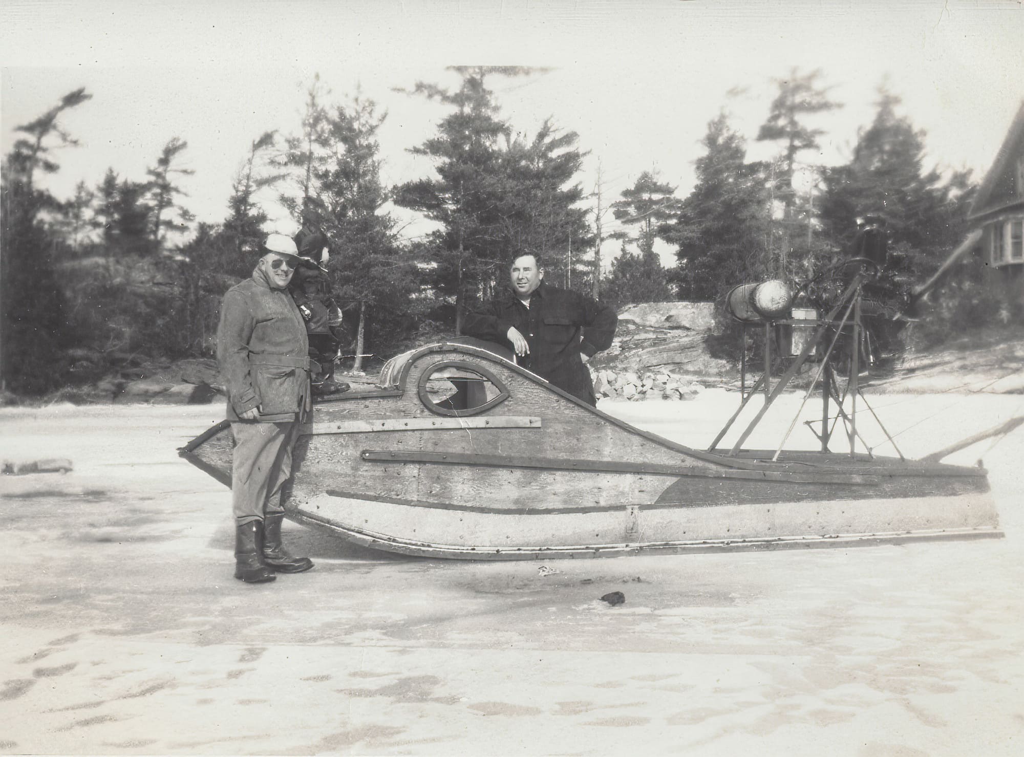 Black and white photo of two men standing around a scoot on the ice